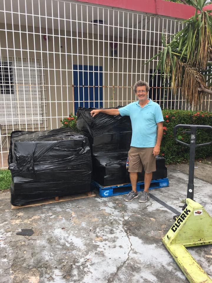 Mr. Jose Galindez standing next to black-wrapped pallets on blue pallets with a Clark pallet jack, outside Alianza's building