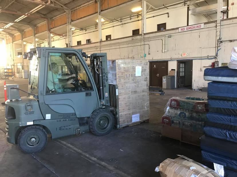 U.S. Air Force Hyster forklift moving a pallet of Kinnikinnick boxes inside the hangar, water pallets stacked nearby